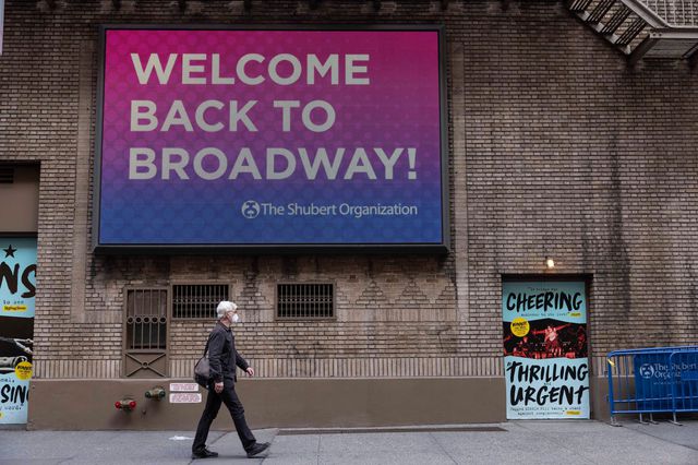 A photo of a person walking past a sign reading "Welcome Back To Broadway"